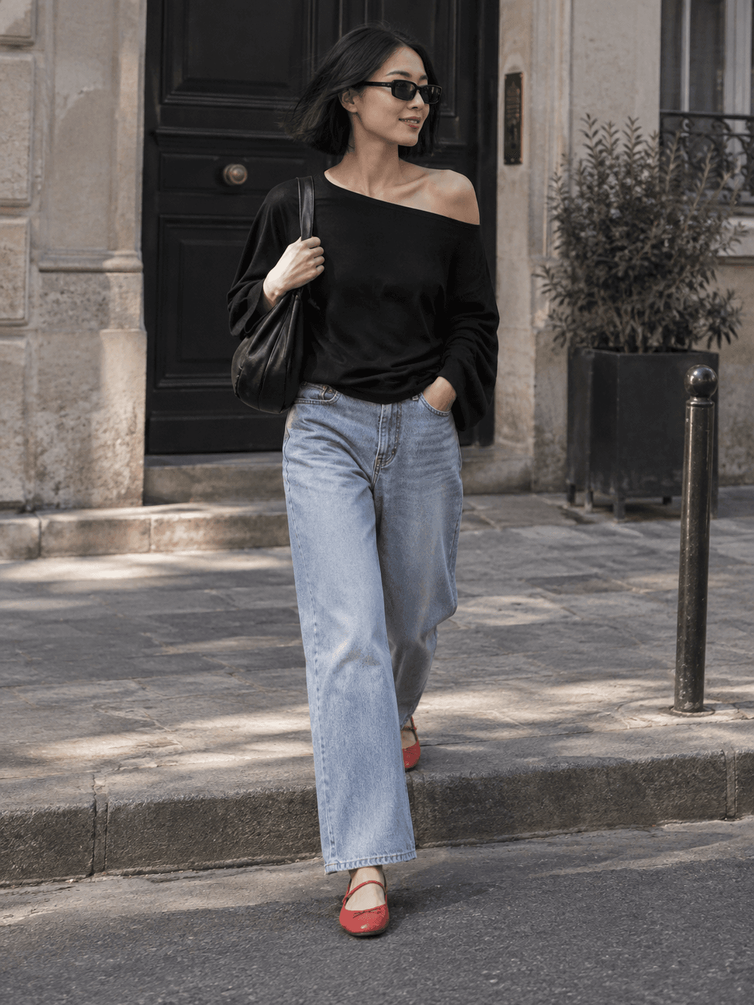 AI styling illustration of a fictional adult woman wearing blue jeans, an asymmetric black top and red ballet flats on a city pavement.