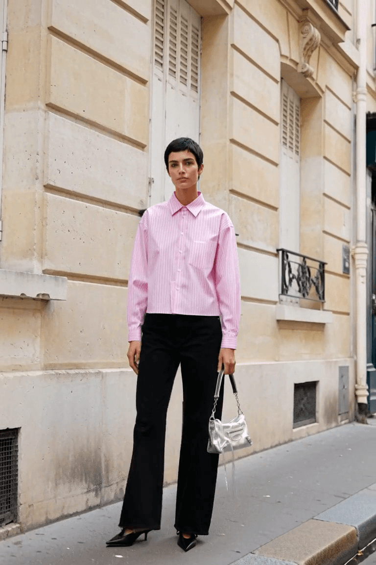 AI styling film of an adult woman in a pink striped boxy shirt, black wide-leg jeans and pointed black mules carrying a small silver bag.