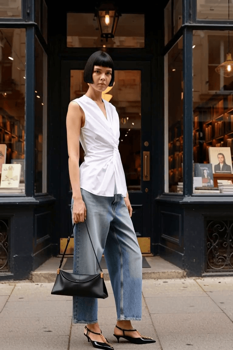 AI styling film: Adult woman in a white gathered blouse, blue barrel jeans, black pointed slingbacks and slim black bag.