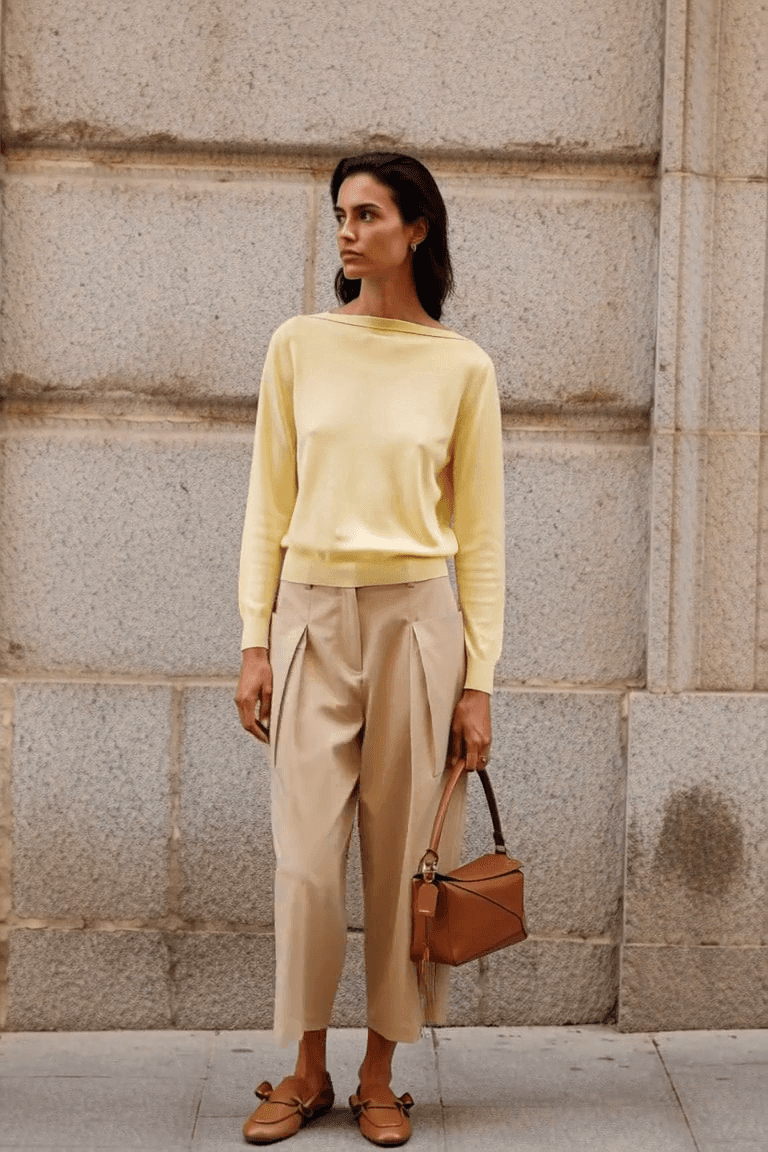 AI styling film of an adult woman in a pale yellow sweater, cropped beige trousers and brown loafers carrying a brown Puzzle-style bag.