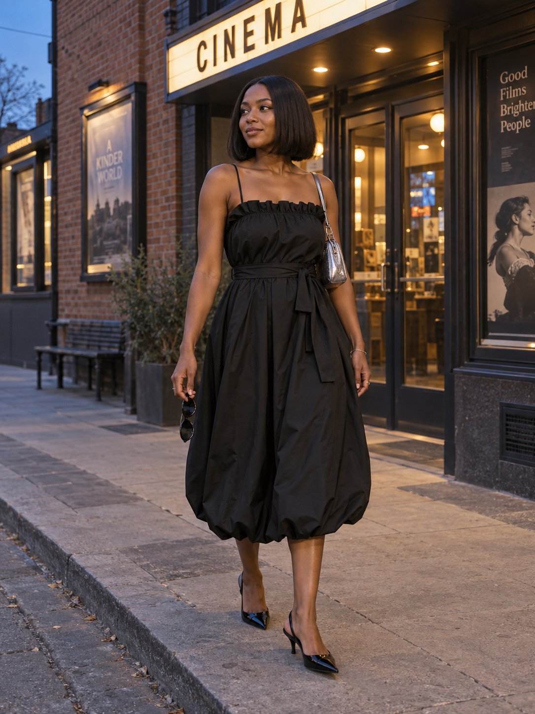 AI styling illustration of a fictional adult woman wearing a gathered black midi dress with a silver bag and black slingbacks outside a cinema.