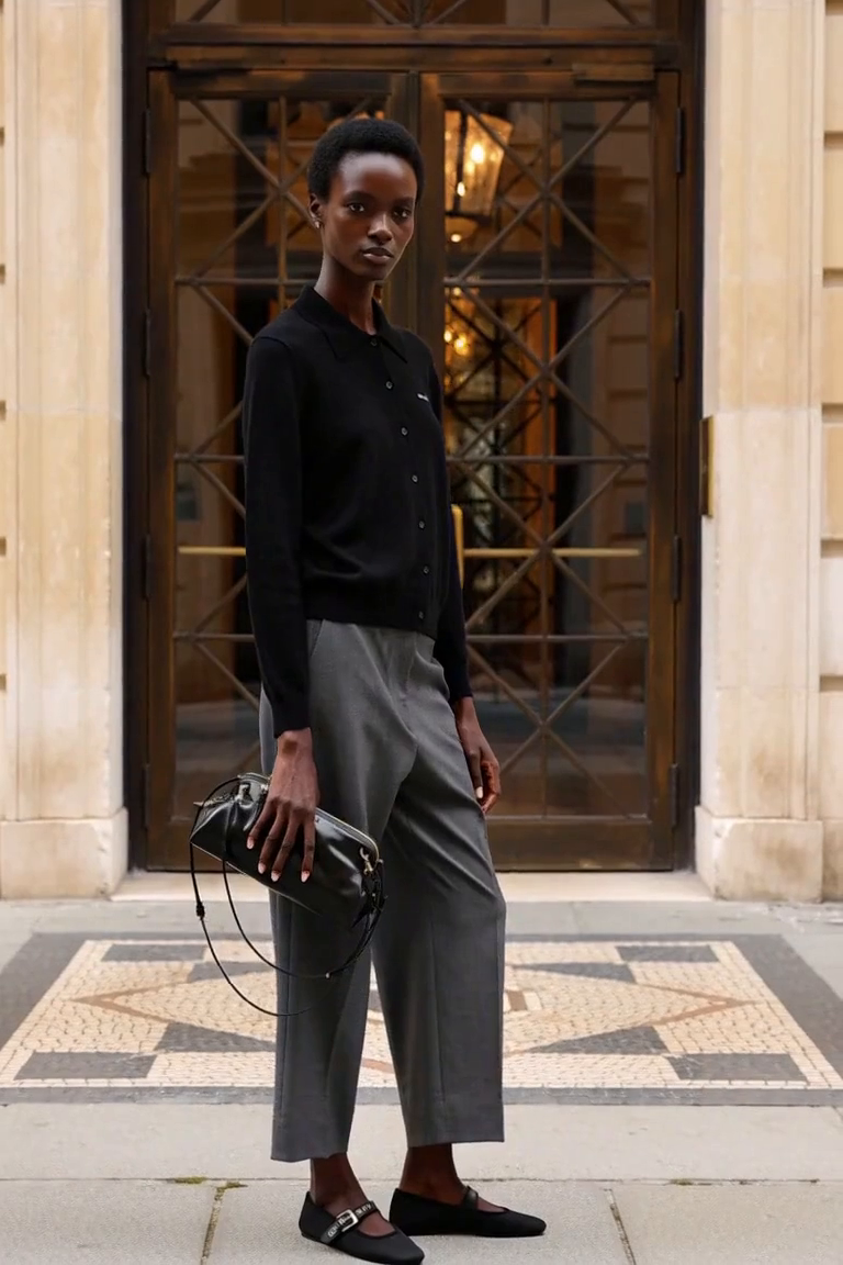 AI styling film: Adult woman in a black collared cardigan, grey trousers, black Mary Jane flats and a shiny black clutch.